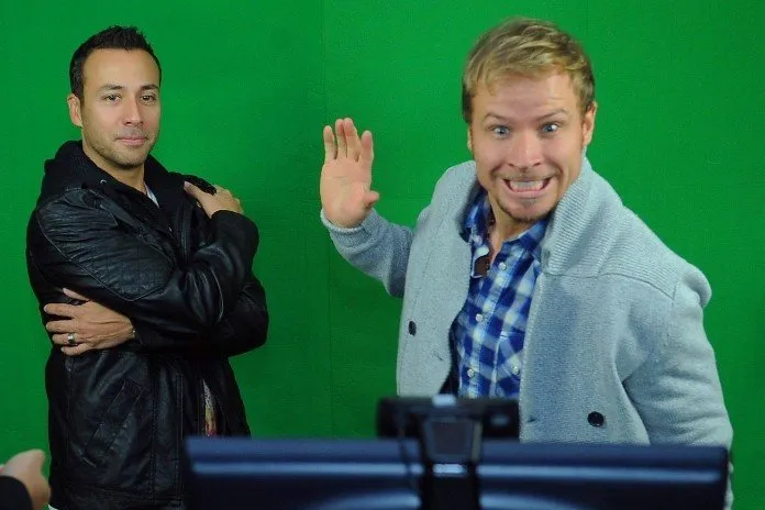 Two men are standing next to each other in front of a green screen.