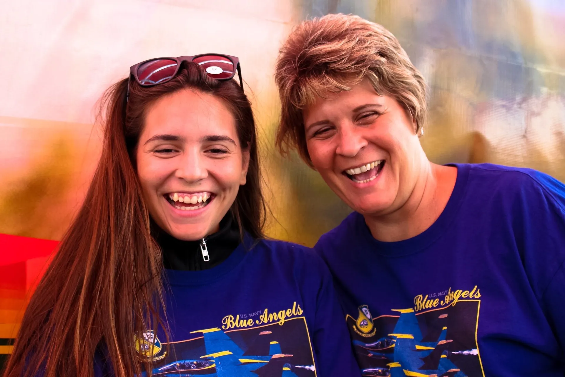 Two women wearing blue angels shirts are smiling for the camera