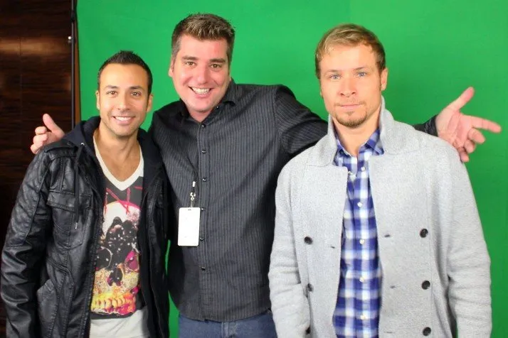 Three men are posing for a picture in front of a green screen