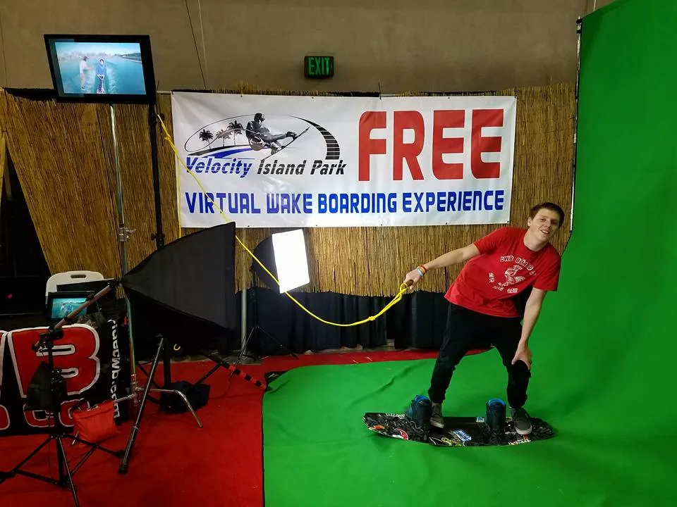 A man is standing on a surfboard in front of a sign that says free virtual lake boarding experience